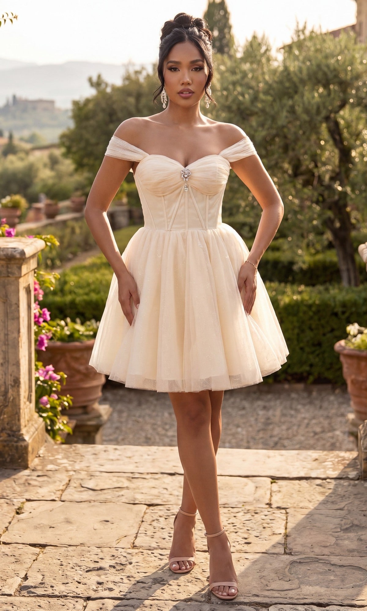 A woman stands outdoors on a stone path, surrounded by greenery and distant hills, wearing the Chicas C382 short homecoming dress in champagne—a flattering, off-the-shoulder fit-and-flare design with a sweetheart neckline—paired with heels.